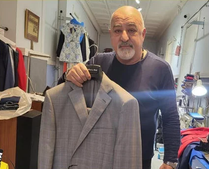 Gregory holding a grey plaid suit jacket on a hanger in the shop